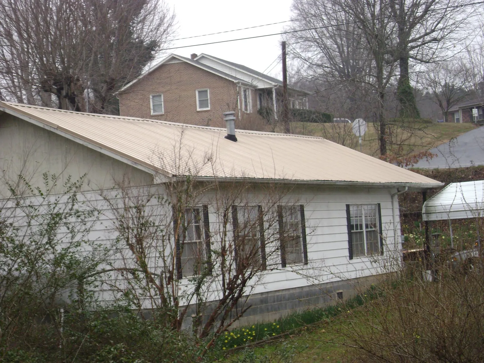 Tan metal roof on a white sided house set into a hillside — Commercial Roofing by Roofing Brothers in Oak Grove