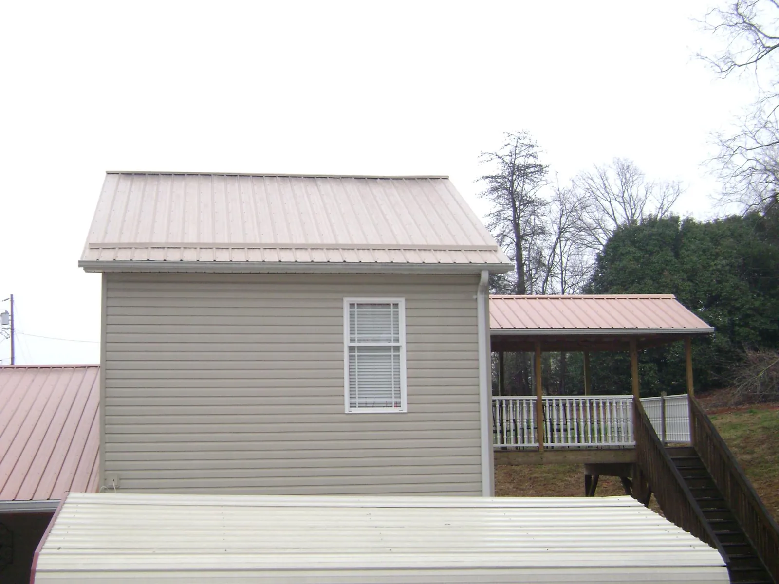 Tan metal roofs on a two story addition and attached porch, from a Roof Replacement job in Oak Grove